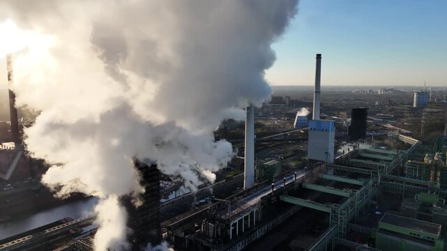 Drone advances through shifting smoke layers that alternately hide and reveal the coking plant below