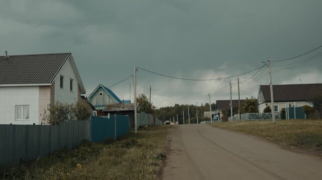 A typical street of an Eastern European village with private houses, poles with wires.