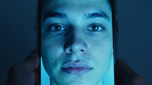 Starting hands moving phone closer for close-up in dim room with blue light, showing male face