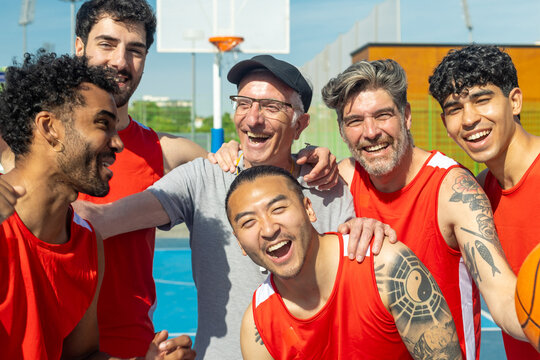 Diverse male basketball team laughing on outdoor court