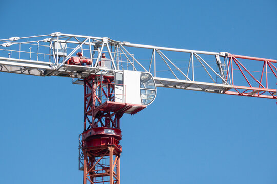 Modern tower crane cabin close up against blue sky. Red and white construction crane machinery detail with copy space.