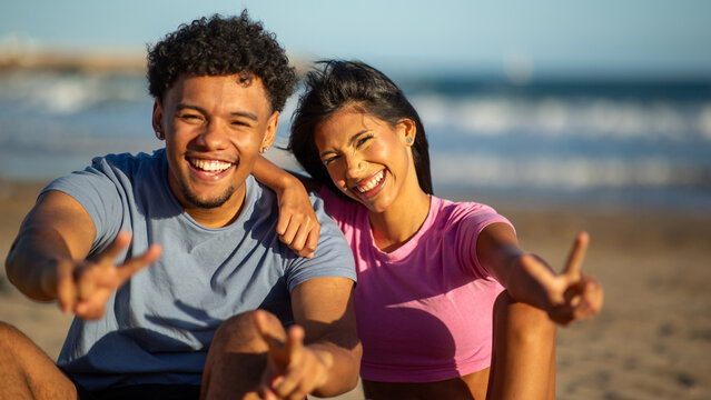 Happy young couple making peace sign at beach
