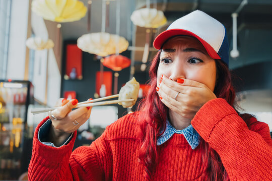 Young woman covering mouth, looking disgusted with dumpling on chopsticks. Experiencing food aversion or allergy reaction