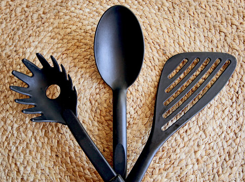 Kitchenware: black plastic ladle for soup and sauce, fork to serve spaghetti and kitchen spatula,  on natural background