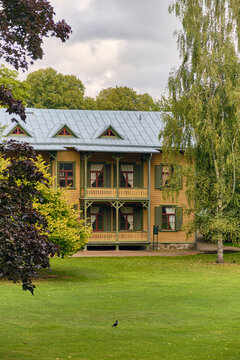 Ronneby, Sweden - 11 September 2025: View of a historic wooden villa in Brunssparken, featuring traditional yellow timber architecture, green shutters, and a balcony, set within a lush park.