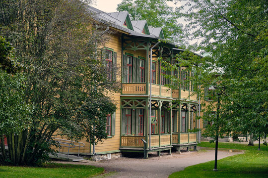 Ronneby, Blekinge County, Sweden - 11 September 2025: View of a historic yellow wooden villa with green trim and balconies in the lush Brunssparken park.