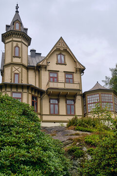 Ronneby, Sweden - 11 September 2025: View of a historic wooden villa with an ornate tower and intricate trim situated within the lush gardens of Brunssparken under a cloudy sky.