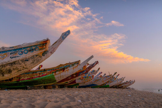 Fishing boats on sandy shore of Port de Peche in Nouakchott, Mauritania at sunset highlight traditional maritime life in West African capital.
