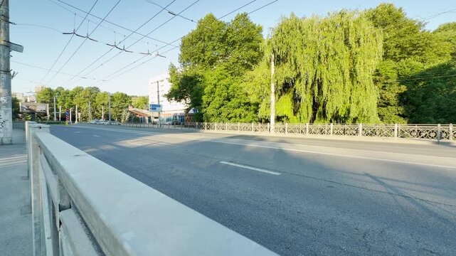 A wide asphalt road lies empty across a sunny bridge in Simferopol, Crimea. The lush green trees create a beautifully peaceful, calm, and serene feeling on this quiet summer morning.