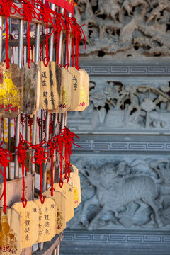 Taipei, Taiwan - 15 January 2026: View of wooden prayer plaques with red strings hanging in a temple with intricate stone carvings in the background.