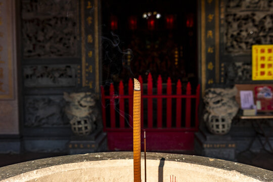 Taipei, Taiwan - 15 January 2026: View of a burning incense stick in a stone burner at a traditional temple with ornate stone carvings and red railings in the background.