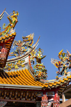 Taipei, Taipei City, Taiwan - 15 January 2026: View of a traditional temple roof adorned with colorful dragon and deity sculptures against a clear blue sky.