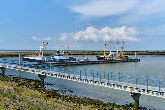Den Oever, Netherlands - 18 May 2026: View of the old harbor featuring fishing vessels and the Navy diving vessel HNLMS Cerberus docked at the pier under a blue sky with white clouds.