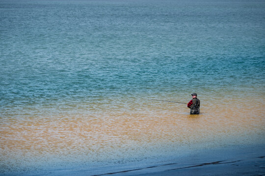 Sveitarfelagid Arborg, Iceland - 06 June 2026: View of a fisherman in waders standing in the colorful water of the Olfusa river estuary with distinct blue and sandy tones.
