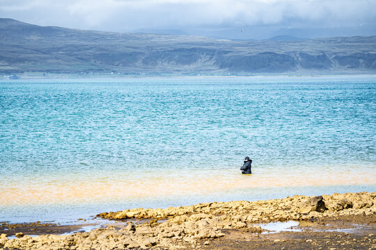 Sveitarfelagid Arborg, Iceland - 06 June 2026: View of a fisherman standing in the colorful waters of the Olfusa river estuary with mountains in the background.