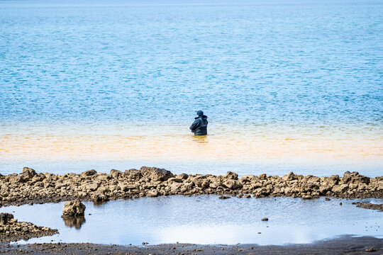 Sveitarfelagid Arborg, Iceland - 06 June 2026: View of a fisherman standing in the colorful waters of the Olfusa river estuary with distinct blue and yellow sediment bands.