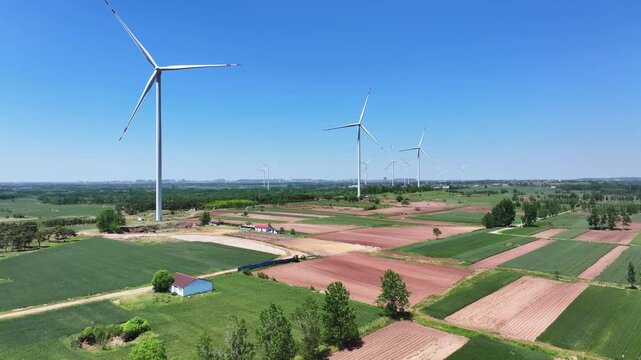 Multiple wind turbines standing in open farmland under clear blue sky