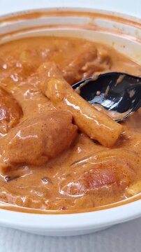 Close-up of a rice cake lifted from a rich, creamy rose tteokbokki bowl.