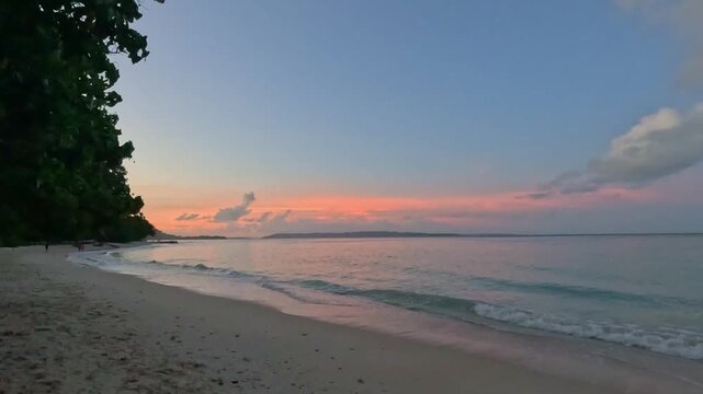 Scenic view of Kalapathar Beach in Havelock Island, Andaman, featuring turquoise ocean waves crashing against unique black rocks and soft white sand under a clear blue sky.  