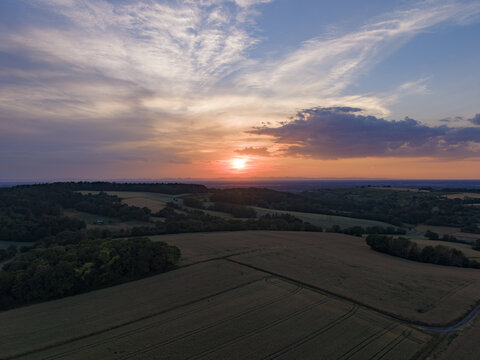 Aerial view of rolling agricultural fields and dense forests under a vibrant sunset sky in Weingarten, Baden-Wurttemberg, Germany.
