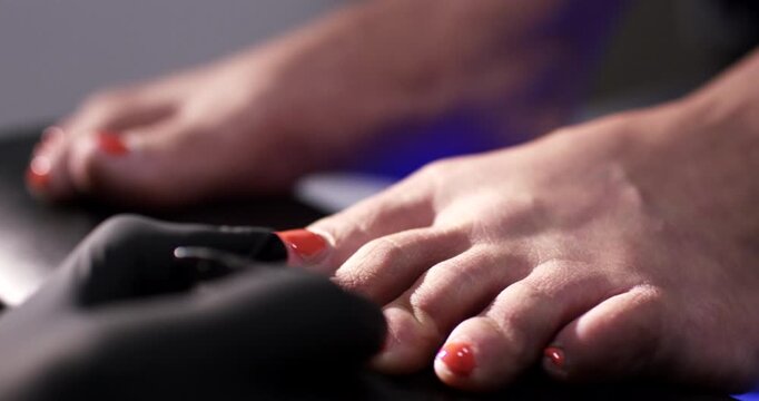 Close up of toes receiving detailed pedicure treatment with orange nail polish