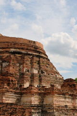 Fototapeta premium Close up view of the ancient red brick base of a stupa ruin at Wat Kudi Dao in Ayutthaya, Thailand. The historic architecture features weathered white stucco details under a bright cloudy blue sky