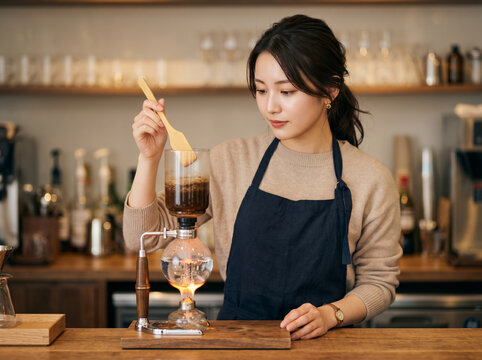喫茶店で竹べらを使ってサイフォンコーヒーを混ぜる女性