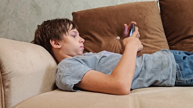 A teenage boy on the couch with his phone, addicted to gadgets. Mental health, mobile phone and boy unhappy on sofa. Scrolling teenager on the phone. gen z boy with technology