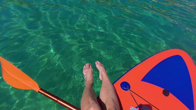 POV video of legs stretched out on a stand up paddle board drifting across emerald and turquoise Adriatic Sea water near Ba&scaron;ka on Krk Island, Croatia