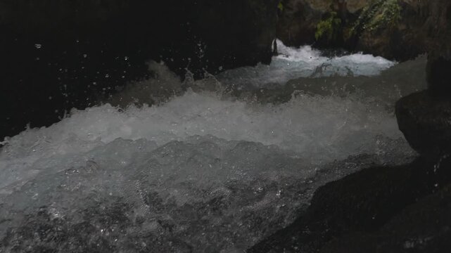 View on fast moving stream of mountain river. Powerful flood broking against stony surface splashing crystal clear water. Cool refreshing creek running in rocky terrain. Slow motion Close up