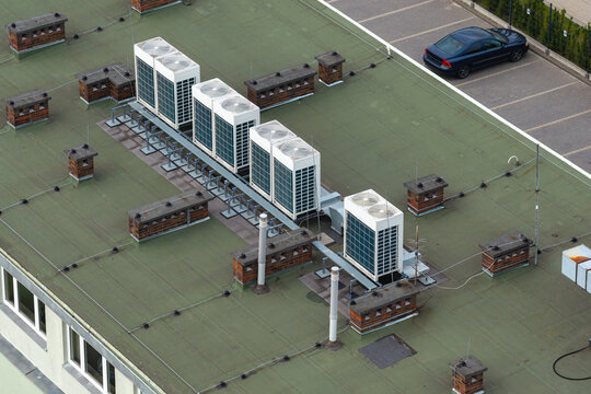 Aerial view of modern HVAC air conditioning units installed on a green rooftop with brick chimneys and a parked car visible below in Warsaw, Masovian Voivodeship, Poland.