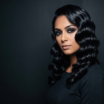 Woman with voluminous wavy black hair and dramatic smokey makeup wearing a black top against dark background. Perfect for beauty, fashion, or elegant portrait design projects.