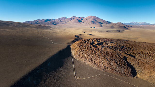 Aerial view of the arid volcanic landscape near Tolar Grande, with a winding dirt road cutting through desert terrain and distant mountains in Tolar Grande, Salta Province, Argentina.