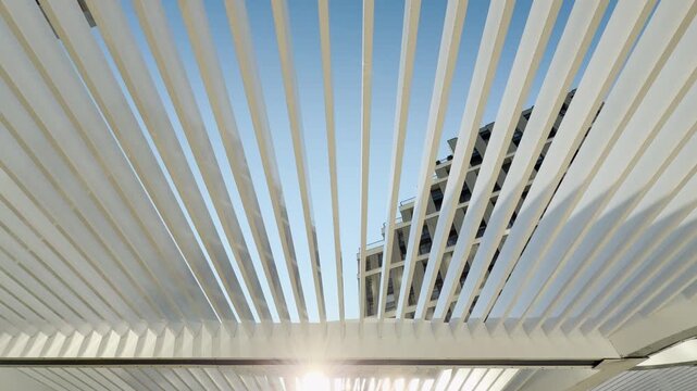 White pergola slats frame a modern building in Simferopol, Crimea. They cut across the clear blue sky, creating an organized and peaceful geometric view that feels clean and refreshing.