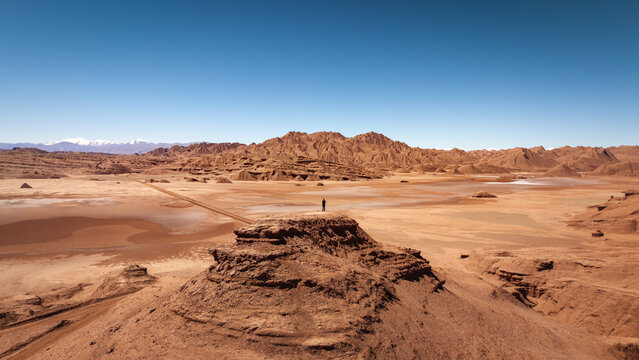 Aerial view of the arid desert landscape with a person standing on a rocky outcrop under a clear blue sky in Tolar Grande, Salta Province, Argentina.