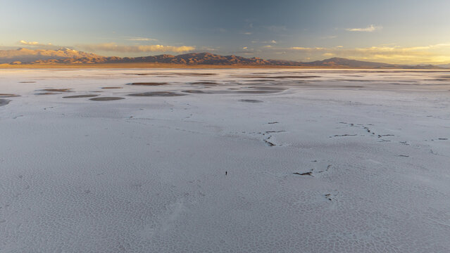 Aerial view of the vast white salt crust of Salinas Grandes with a lone person standing in the center under a golden sunset sky in La Poma Department, Salta Province, Argentina.