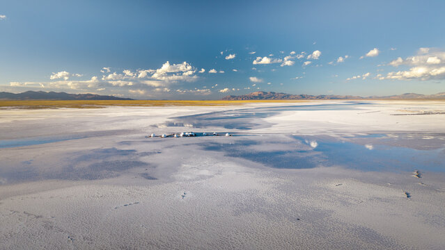 Aerial view of Salinas Grandes salt flat with shallow water pools reflecting the blue sky and distant mountains in La Poma Department, Salta Province, Argentina.