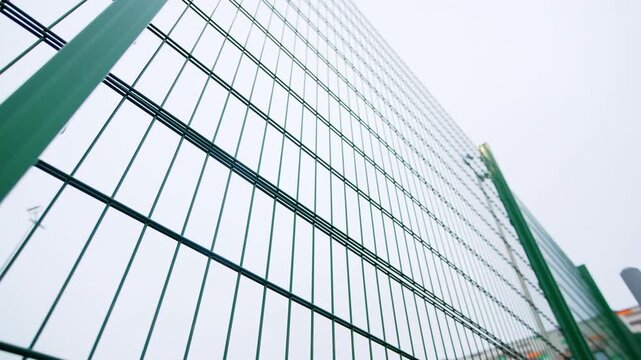 Professional mesh fencing surrounds contemporary educational facility. Overcast sky and geometric architecture create clean urban look