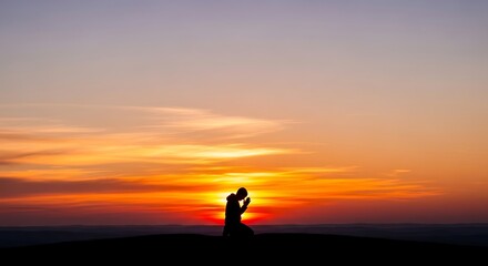 Obraz premium Silhouette of a person kneeling in prayer against a colorful sunset sky