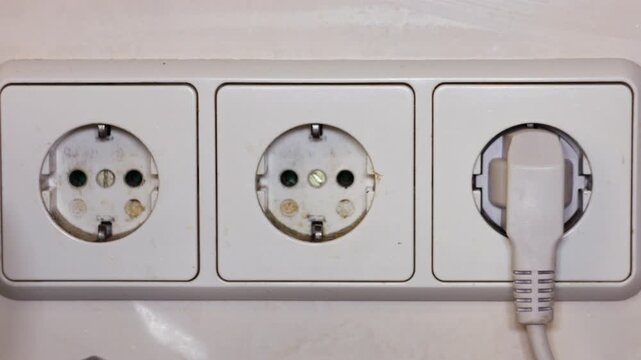 Close-up of Hand Plugging Electrical Cable into a Triple Wall Power Socket