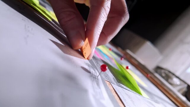 Slow-motion close-up of a detective placing a fresh note onto an investigation board. Suggests breakthrough discoveries, developing leads, and strategic case analysis.