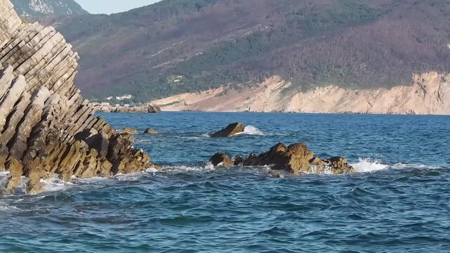 Scenic view of blue sea waves crashing and splashing against unique layered geological rock formations on the coast of Petrovac, Montenegro