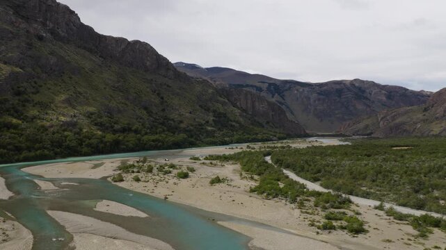 R&iacute;o de las Vueltas flows through braided channels near El Chalt&eacute;n, Santa Cruz, Argentina, bordered by gravel bars, shrubland and rugged Andean mountains, drone forward flyover shot.