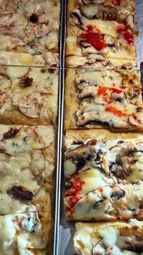 Vertical close-up view, artisan mushroom pizza al taglio slices and other delicious flatbread options on display trays