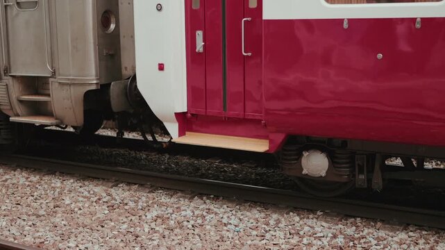 Closeup of train carriage coupling mechanism and wheels between red and silver carriages on tracks