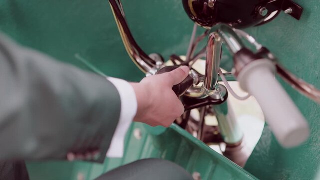 Suited man gripping chrome handlebar of vintage turquoise tricycle vehicle at wedding