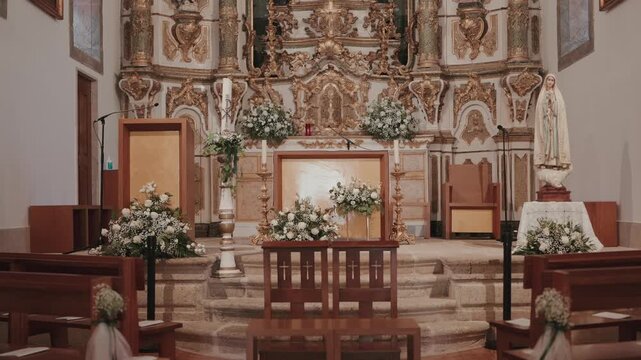 Ornate baroque gilded retable altar with white floral arrangements candlesticks and Virgin Mary statue for wedding
