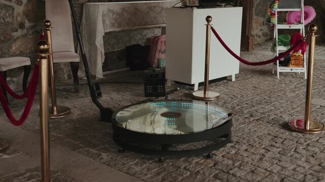 360 spinning photo booth with gold stanchions and red ropes on stone floor indoors