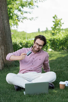 Stylish man enjoying summer vibes while shopping online in a serene park setting
