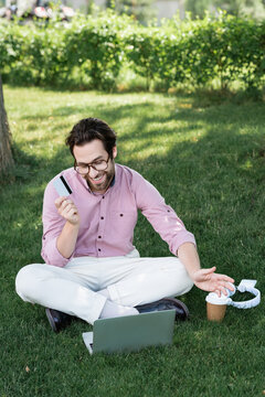 Stylish man enjoying summer day while working on his laptop in a lush green park